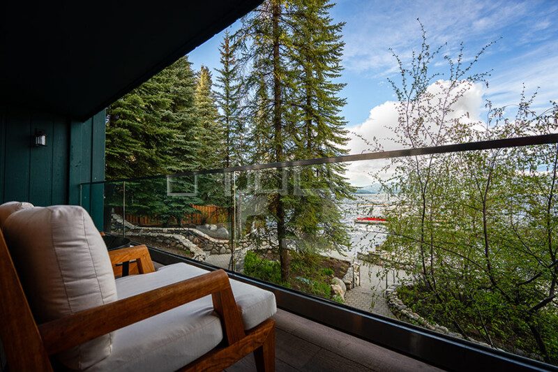 A balcony with a lounge chair looking through the pines to the lake